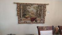 Front view of castle scene tapestry hanging on wall with visible tassels and part of chairs below