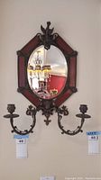 Wall mounted mirror with ornate red and bronze finish frame, eagle motif on top, and two curved candle holders extending from base.