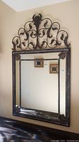 Full view of rectangular wall mirror with ornate decorative wrought iron frame and scrollwork crest.