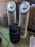 View of two tall white Honeywell HHT-217 air purifiers and one black Media Therapeutics air purifier from the front showing control panels and vent grills