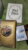 Two Bibles, one white cover with decorative border and one brown cover with religious image, along with DVD case partially visible