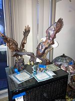 Three eagle sculptures displayed on a glass top dark chest, with certificates of authenticity laid out in front of each piece.