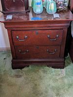 Full front view of the Broyhill wooden nightstand, showing two drawers with metal handles and keyholes, surface wear visible.
