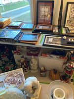 Assorted framed pictures on a table with some Christmas figurines and wreaths placed below showing diverse holiday decor items present in the lot.