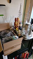 Christmas decorations lot including silver lantern, spiral tree decorations with crystal tinsel, various holiday figurines, glass candle holders, and boxed crystal tinsel garlands.