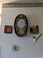 Oval battery operated wall clock mounted on wall flanked by two inspirational ceramic tiles with quotes