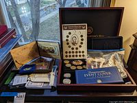 Overview of wooden display box with multiple coin sets, pouches of coins, and colorized $2 bill