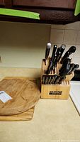 Photo showing the wooden Six Star Cutlery block filled with various black-handled knives and two wooden cutting boards beside it.