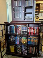 Full view of wooden cabinet with glass-paneled doors containing DVDs, VHS tapes and CDs.