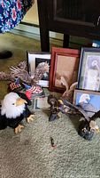 Overview of eagle-themed items including a plush eagle, eagle sculptures, framed art, and collectibles arranged on carpeted floor.