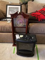 Photo showing electric heater fireplace in front of dark wood framed wall clock on carpeted floor