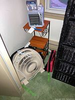 View of two fans, side table, and red and white first aid kit bag on green carpet