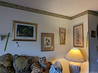 Wall display of four framed art pieces above couch with large floral pillows and a lamp, showing Monet print, bird print, and two floral prints.