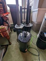Two black Air Innovations humidifiers with long towers, control knobs, and power cords; placed on carpet next to furniture.