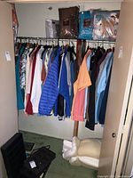 Closet rack with assorted men's shirts, jackets, sweaters in various colors including blue, orange, and white; items appear worn.
