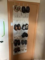 Full view of men's shoes displayed on a white fabric over-the-door shoe rack hung on a wooden door. The rack holds multiple pairs of shoes in various colors and styles.