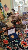 Photo showing a mix of resin and brass eagle and moose figurines on floral cloth with small American flags and collectible coins visible.