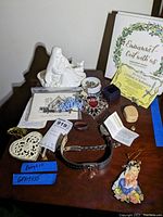 Overview of lot items on wooden surface including figurine, paper ephemera, jewelry, and cross ornament