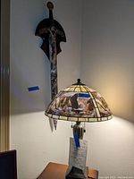 Photo showing the wooden commemorative sword with eagle design hanging on wall behind the stained glass eagle lamp sitting on a wooden table.