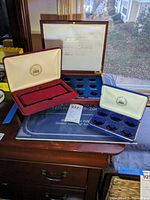 Photo showing multiple coin cases arranged on a dresser including burgundy and blue velvet-lined cases, with slots to hold quarters, alongside a quarter collection album below.