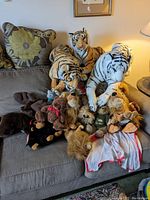 Couch with various large and medium-sized stuffed animals including tigers, lions, bears, monkeys.