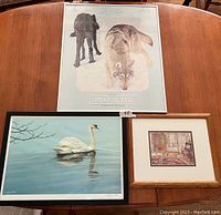 Three framed prints on a wooden table including Timber Wolves, swan, and interior scene.