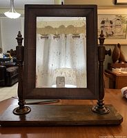 Front view of antique wooden dresser top mirror showing the foggy reflective surface and wooden swivel supports.