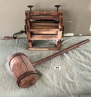 General view of the antique wooden wringer washer attachment and large wooden mallet placed on a surface.