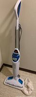 Full view of Bissell steam mop standing upright with power cord wrapped around, showing the mop head and handle.