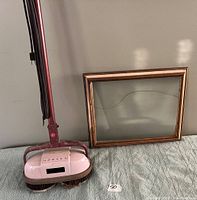 Photo of pink and maroon Hoover floor polisher standing upright beside empty wood frame with UV blocking glass.