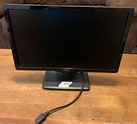 Front view of Dell LCD monitor with power and VGA cable attached, placed on wooden table.