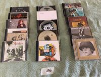 Photo of 16 music CDs by various artists arranged in four stacks on a cloth surface.