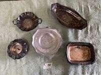 Top-down view of four tarnished silver plated trays and one aluminum tray arranged on cloth background.