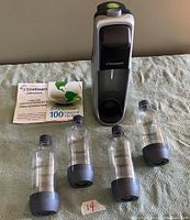 Full setup of SodaStream carbonator machine with four bottles, user manual and flavor guide booklet, laid out on cloth surface.