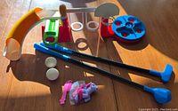 Photo of Tupperware playground set, plastic golf clubs, balls, and My Little Pony toy with comb on a wood surface.
