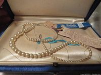 Pearl necklace laid inside original vintage box with satin lining. Box shows wear and some damage. Necklace includes tags.