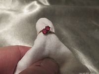 Photo of a yellow gold ring with two round red faceted rubies held on a white cloth.