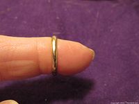 14K gold band on finger showing its width and shape against a purple background.