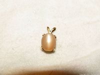 Photo of the 14k yellow gold pendant bezel set with a natural oval cat's eye moonstone on a neutral background.