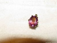 Top-down photo showing the pink tourmaline oval gemstone set in a 14K gold prong setting on a light surface.