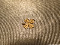Four-leaf clover shaped gold pendant charm on a textured beige background, showing polished gold surface and attachment loop.