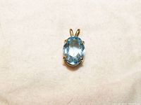 Front view of oval blue topaz pendant set in 14k yellow gold against a light background.