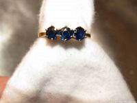 Close-up front view of the yellow gold ring with three round faceted blue sapphires on a white background.