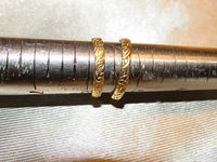 Pair of yellow gold ornate rings shown side by side on a ring sizer tool, highlighting their size difference and detailed pattern around the bands.