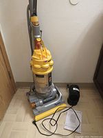 Dyson DC14 upright vacuum with cord, manual, and black bag accessory on floor