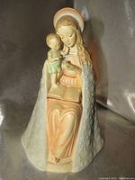 Front view of the porcelain figurine showing Madonna seated with Child on her knee, holding an object and an open book on lap.