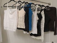Photo showing eight fancy business tops hanging on black hangers on a metal rod, in various colors including white, beige, black, blue, and brown, mostly lace or textured fabric.