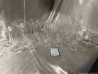 Full view of 24 Galway Irish Crystal glasses in three different styles arranged on a silver fabric background with a matching Galway booklet.