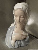 Porcelain bust figurine of the Virgin Mary from a three-quarter profile showing delicate facial expression, matte finish, and pastel blue and white colors.