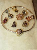 Full view of silver snake chain bracelet with 8 assorted charms laid in a circle on a cream cloth surface.